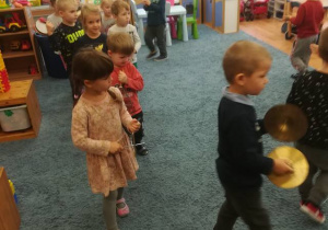 Dzieci chodzą po sali grając na instrumentach perkusyjnych